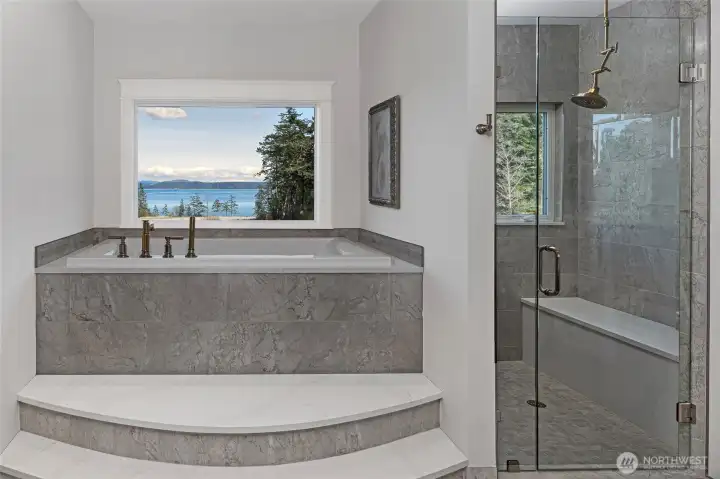 Spa-inspired primary bath with elevated soaking tub framed by picture window, marble tile surround, and sweeping water views toward Mount Baker.
