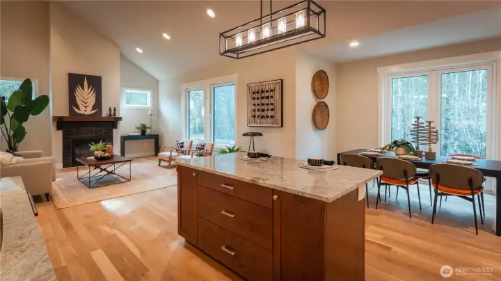 This beautifully designed open-concept space showcases a seamless flow between the kitchen and great room. Vaulted ceilings enhance the sense of volume, while large windows fill the room with natural light. The expansive island offers generous prep space and seating, making it the true centerpiece for gathering and entertaining. The living area is anchored by a cozy fireplace, creating a warm and inviting atmosphere.