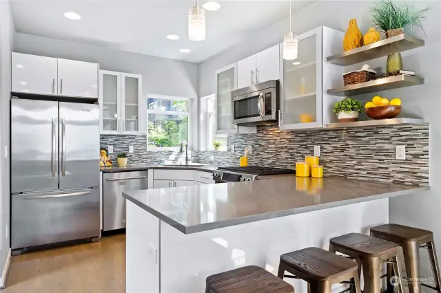 Quartz countertops including a large breakfast bar, and glass tile backsplash enhance this beautiful kitchen.