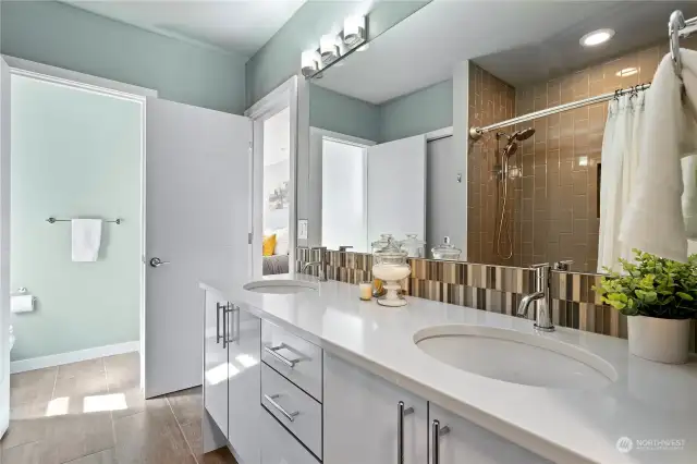 The primary bedroom bathroom has a sleek double vanity with quartz countertop and glass tile backsplash, and a  separate toilet room.