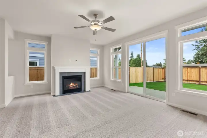 Living room with plenty of natural light featuring cozy gas fireplace with tile surround and ceiling fan.