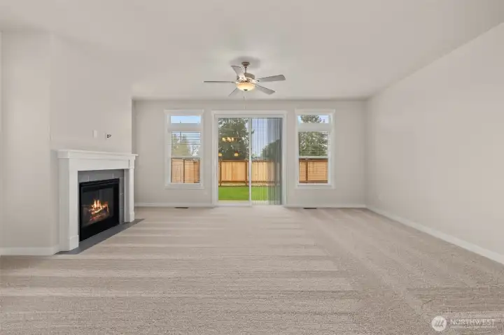 Living room with plenty of natural light featuring cozy gas fireplace with tile surround and ceiling fan.