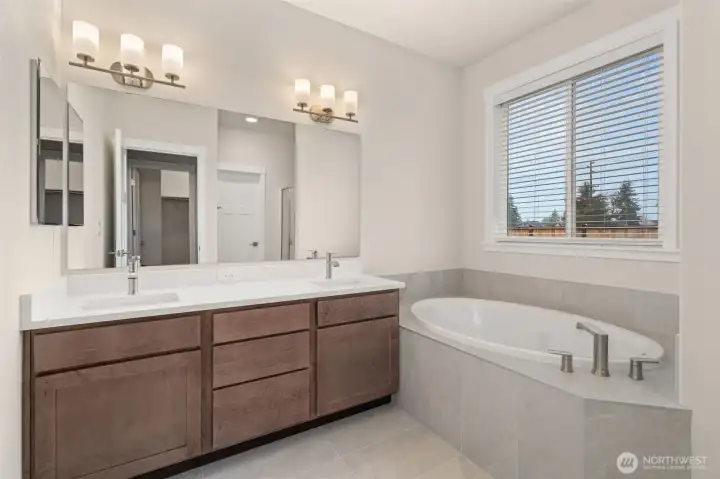 Primary bathroom has a double vanity with undermount dual sinks, tile floor, quartz countertops and a soaking tub with tile surround.