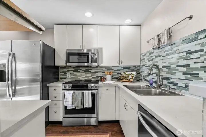 The kitchen is airy, with stainless steel appliances, glass tile backsplash and white wood cabinets