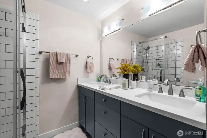 The four piece bath has deep navy cabinets, two sinks, and a lovely tiled shower with glass surround.