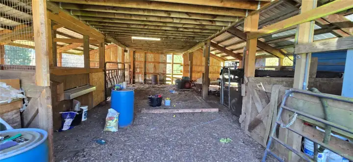 Alley way in barn with finished stall to the right, chicken coop in left corner. Back left is a run in shed style with gate. Additional bays to the right that can be used to enclose more stalls.