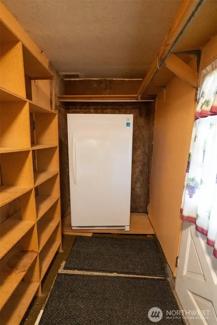 View of your back/carport entry hall, showing the included upright freezer and convenient storage shelves.