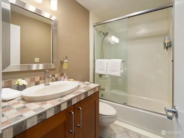 The full bath is well-designed, light and contemporary with a glass shower door and tiled countertop.