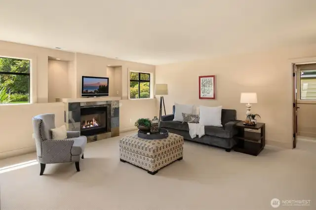 Main floor bonus room features the 1st of the 3 gas fireplaces in the home, as well as beautiful southern facing windows, framing the views of fully landscaped side garden. Door to the right leads to full bathroom, wet bar, and storage/office space area to the right.
