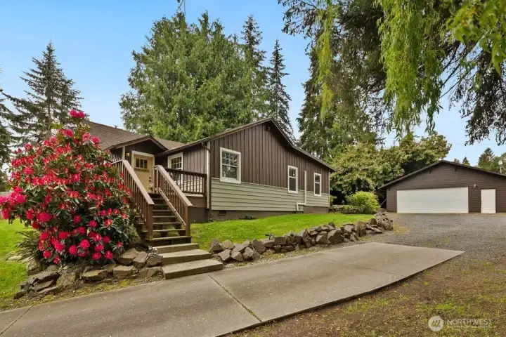 Charming single-story home with mature landscaping, vibrant flowering shrubs, and a detached shop/garage offering extra storage and workspace potential.