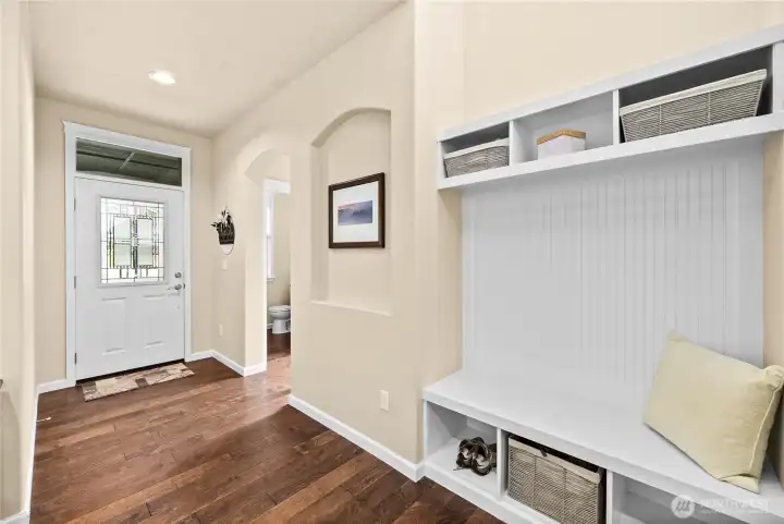 Welcoming entry with rich engineered hardwood flooring, offering a stylish drop zone with built-in seating and storage, nearby half bath, and additional under-stairs storage.