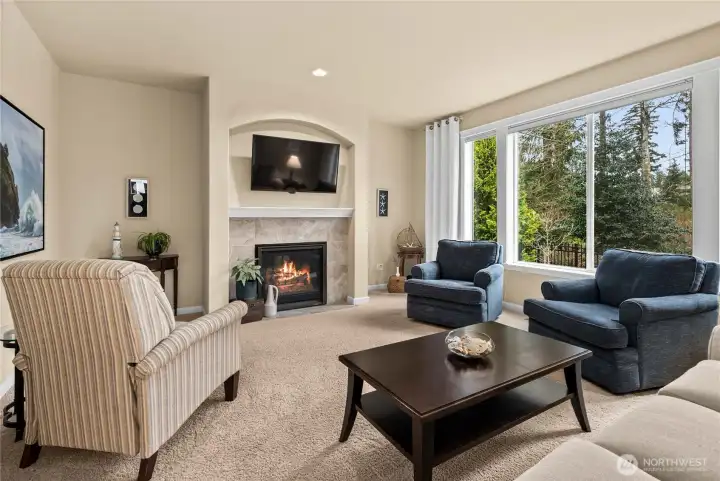 Light-filled living room with expansive windows showcasing gorgeous golf course views and a cozy gas fireplace creating a warm and welcoming gathering space.