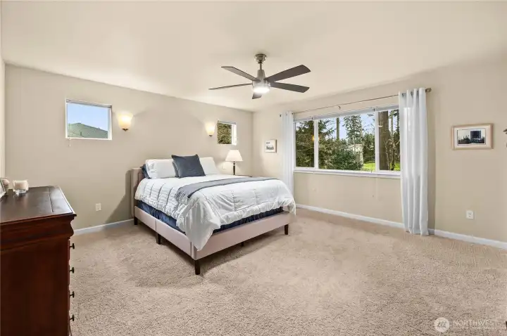 Serene primary suite accessed through elegant French doors, featuring plush carpet, stylish wall sconces, and beautiful golf course views.