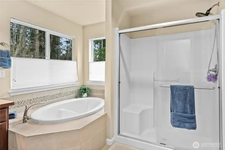 Relaxing corner soaking tub with full tile surround and large windows featuring adjustable shades for natural light and privacy. Walk-in shower with glass doors and molded seating adds comfort and convenience.