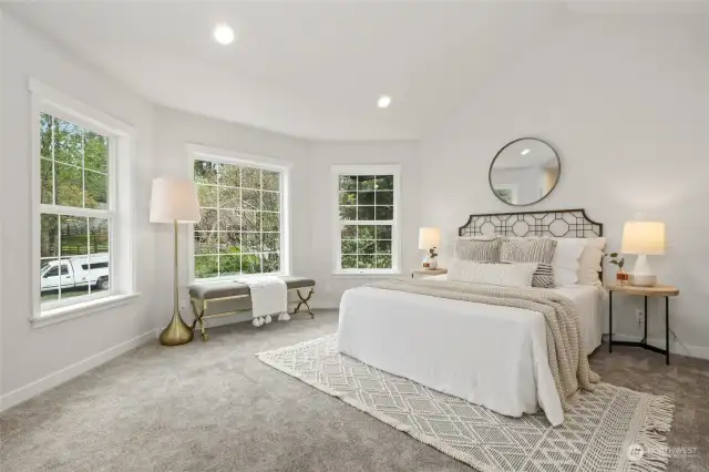 The airy first-floor primary suite is spacious and bright, boasting a bay of windows, vaulted ceilings, a walk-in closet, and additional closets, providing ample storage.