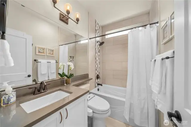 Guest bath with Quartz counters, upgraded fixtures & lighting, oversized tub w/ tile surround & tile floors.