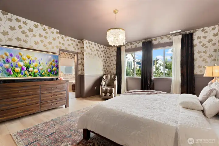 The primary suite offers a moody, color-drenched retreat with elevated design details throughout. Enter through a charming barn door into a private nook before stepping through the double-door entry into the spacious bedroom. Wainscoting and leaf-patterned wallpaper create warmth and texture, while newly added window casings enhance the tailored finish. A statement chandelier from Pottery Barn adds a soft glow and timeless elegance, perfectly complementing the room’s luxurious yet cozy vibe. It’s a restful haven designed with both beauty and serenity in mind.