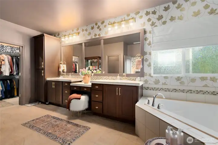 The expansive primary bathroom is both luxurious and practical, offering a spa-like layout with room to truly unwind. It features a large soaking tub beneath a frosted window for privacy and natural light, a walk-in shower, and a separate water closet with a stylish feature wall and added shelving. Dual vanities with updated lighting, new faucets, and elegant brass hardware provide plenty of space for morning routines. Rich cabinetry, a built-in makeup vanity, and a convenient linen closet complete this beautifully appointed retreat.