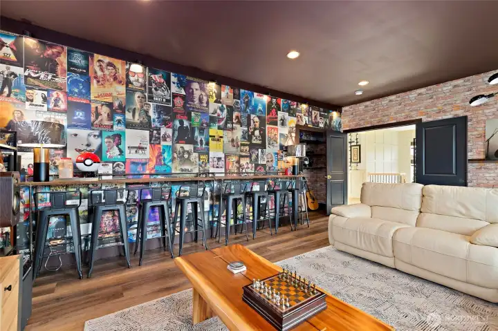 Another look at the upper-level bonus room, where style and functionality go hand-in-hand. High-end custom wallpaper wraps the space, amplifying the moody, cinematic vibe—perfectly complemented by rich, dark LVP flooring. A custom bar-height counter runs the length of the wall for extra seating or entertaining, while ambient and accent lighting create just the right atmosphere. The closet was upgraded with wood-stained shelving to add smart, stylish storage. Whether you're watching a film, hosting game night, or relaxing solo, this space brings elevated comfort to everyday living.