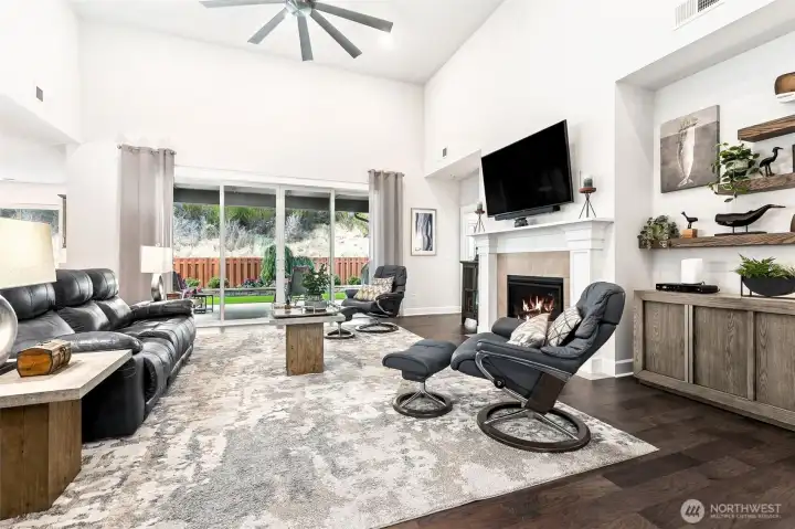 Living room is bright and open with  wall of windows and oversize slider to the yard that opens to the covered patio.  Gas fireplace with mantle, 72" ceiling fan and cathedral ceilings make a statement.  Electrical floor outlets allows you to hide the cords! Handsome space with flexible layout.