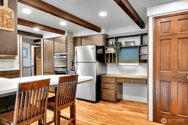 Open kitchen layout with stainless steel appliances, exposed beams, and a built-in desk or coffee station.