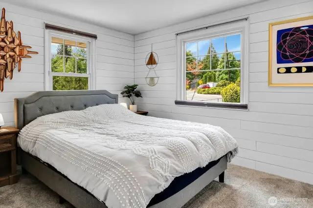 Bright primary bedroom with shiplap walls and large windows.