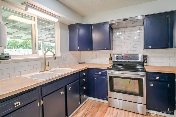 Second kitchen view with window facing back yard with goose neck faucet newly painted cabinets and more laminate wood flooring for low maintenance care