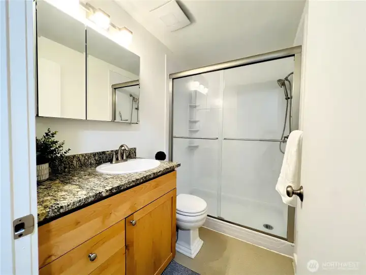 This spacious bathroom features granite counters and a glass shower enclosure.