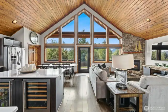 Spacious great room with soaring ceilings, a cozy gas fireplace, quartz counters, custom lighting, and dual beverage fridges.