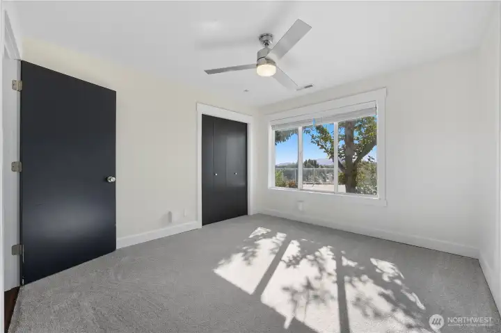 Bedroom 2 -   Spacious secondary bedroom with tree-lined views, sleek ceiling fan, and modern black accent doors for a refined touch.