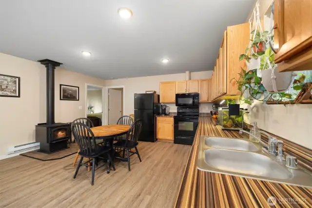 Main living area including kitchen and dining and new wood stove with view into Primary Bedroom (left) and 3rd bedroom (right)