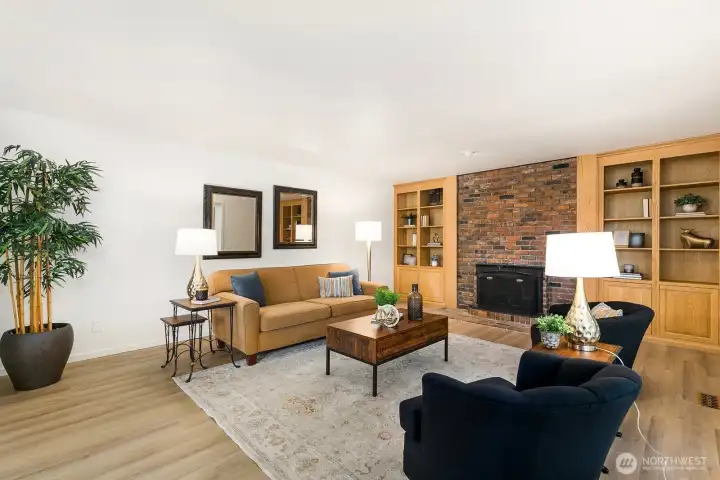 Spacious living area with brick fireplace, built-in shelving, and large picture windows.