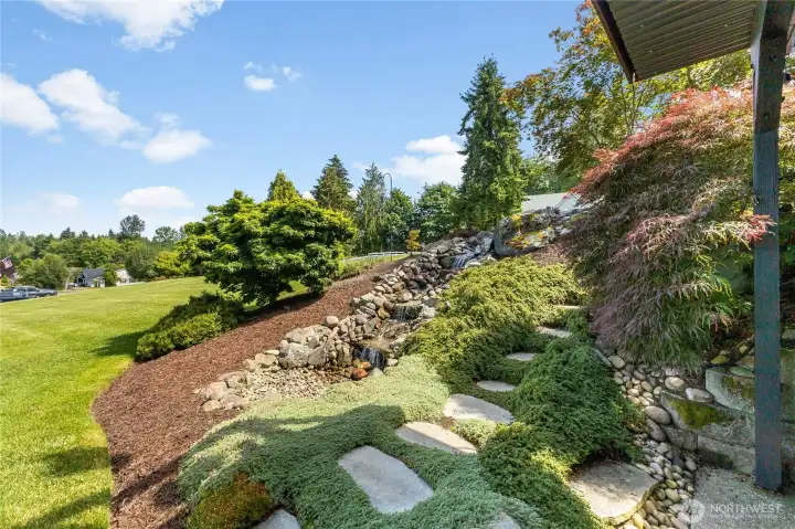 Waterfall feature has low voltage lighting and auto fills. The stepping stones connects both lower level and upper. Tastefully landscaped Waterfall feature has low voltage lighting and auto fills. The stepping stones connects both lower level and upper. Tastefully landscaped