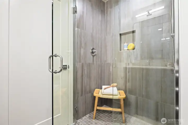This luxe walk-in shower features oversized tiles and glass doors, a built-in niche, and calming design touches.