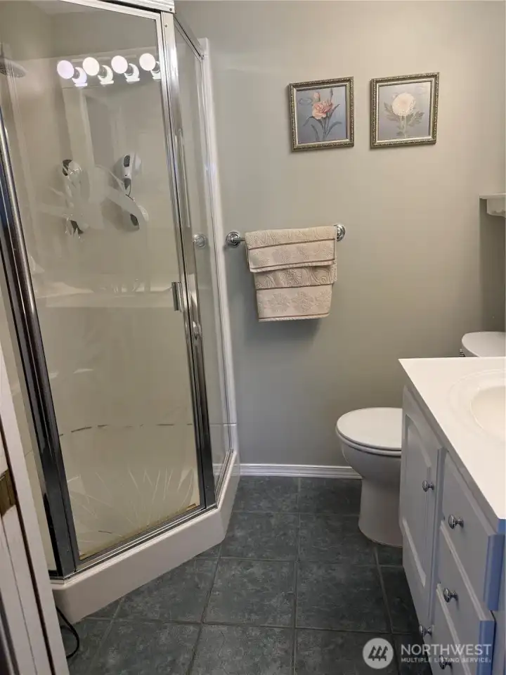 Primary bath has spacious corner shower, tile flooring and a corner cabinet.