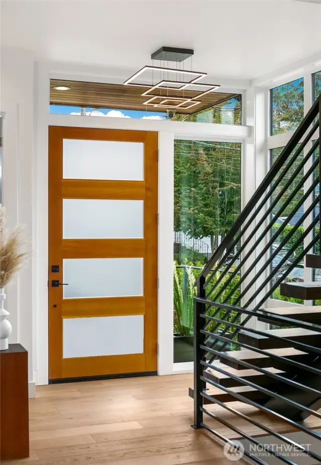 A warm welcome at 4015A NE 56th St.  The main residence opens with a striking blend of natural wood and frosted glass, setting a modern yet inviting tone. Tall sidelights and transom windows flood the foyer with natural light, while a custom steel stair rail hints at the architectural refinement found throughout.