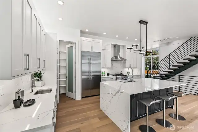 Culinary elegance meets functional design  An expansive chef’s kitchen, anchored by a waterfall-edge quartz island, is outfitted with top-tier Bosch appliances—including a 36” five-burner gas cooktop and counter-depth French-door refrigerator. A walk-in pantry and appliance garage keep essentials within reach but out of sight, while full-overlay cabinetry offers generous storage with sleek, modern lines.
