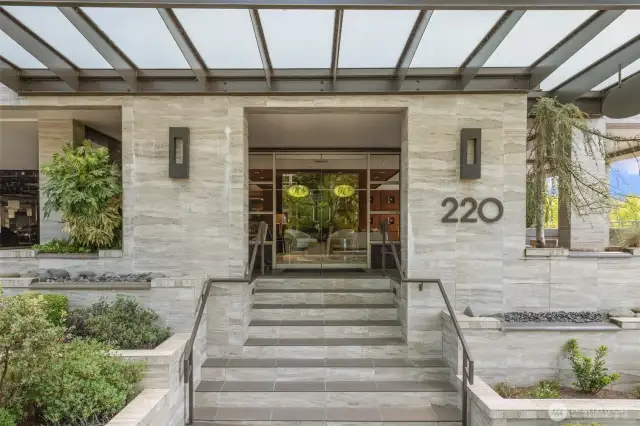 Welcome to 220 1st Street—a grand first impression with this sleek, modern entry. Framed by lush landscaping and contemporary stonework, the covered entrance leads into a secured building with an elegant lobby just beyond the glass doors.