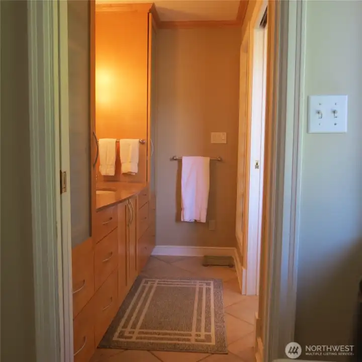 Entrance into primary bath via pocket door. Sink to the left and shower and toilet out of frame to the right. Also features radiant floor heat.