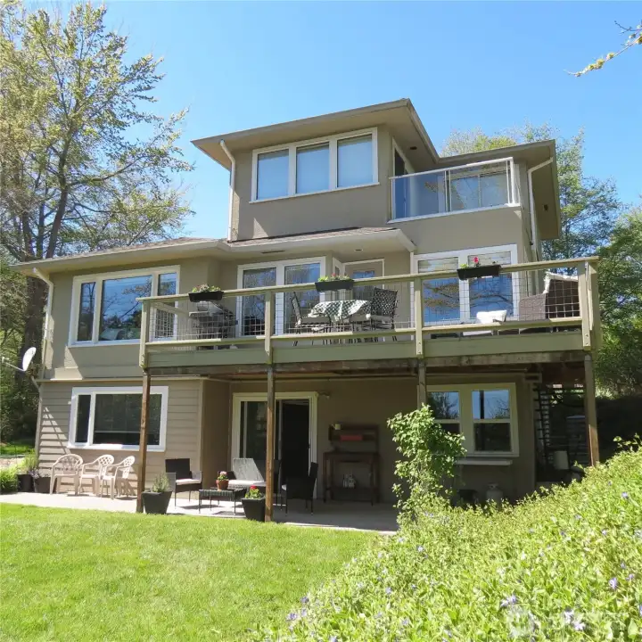 Back of the house showing a peaceful yard, the covered lower patio/seating area and the private daylight basement entrance.