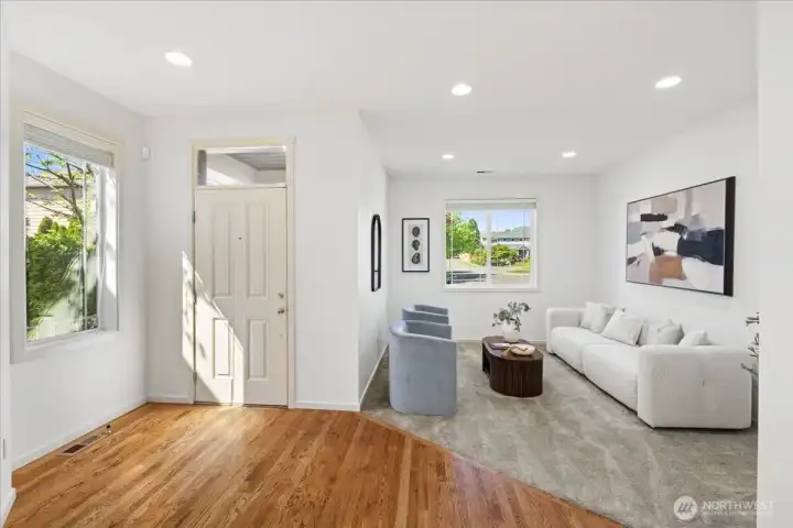 Open front entry transitions seamlessly into the living room, featuring hardwood flooring, plush carpeting, and abundant natural light.