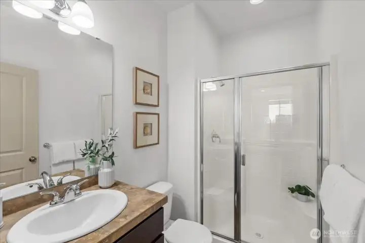 Main-level bathroom featuring a vanity, large mirror, and glass-enclosed shower. Clean finishes and functional layout offer convenience for guests or everyday use.
