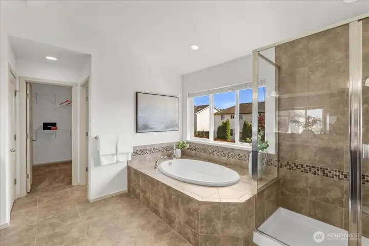 Spa-inspired primary bathroom featuring a soaking tub, separate glass-enclosed shower, tile flooring, and a large window that brings in abundant natural light. Thoughtfully designed with a spacious layout and direct access to the adjoining walk-in closet.