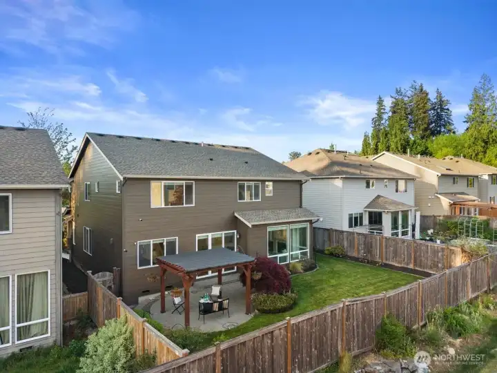 Elevated exterior view showcasing the fully fenced backyard, landscaped garden beds, expansive lawn, and covered patio. Highlights the home’s outdoor living space and well-maintained grounds.