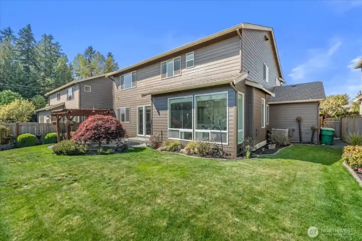 Ground-level view of the spacious backyard featuring lush lawn, mature landscaping, and multiple outdoor seating areas. Fully fenced setting offers privacy and room to enjoy outdoor living.