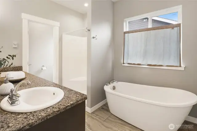 Primary bath with luxurious soaking tub, separate shower, and toilet closet, dual vanity with same cabinetry with granite countertops, and tile floors.