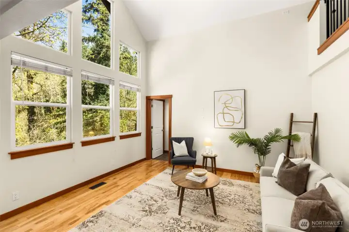 A dramatic wall of windows fills this living space with natural light, highlighting the home’s soaring ceilings. Surrounded by peaceful greenery, the view brings a sense of privacy and connection to the outdoors that’s hard to find.
