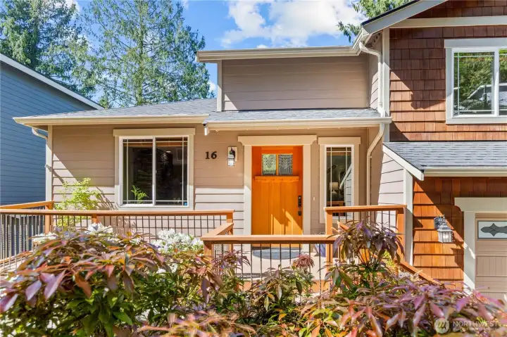 Welcoming front entry with covered deck access and landscaped approach surrounded by established greenery.