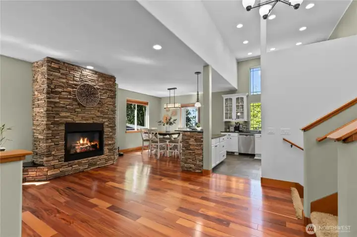 Spacious main living area with rich hardwood floors, soaring ceilings, and a floor-to-ceiling stone fireplace creating a warm focal point.