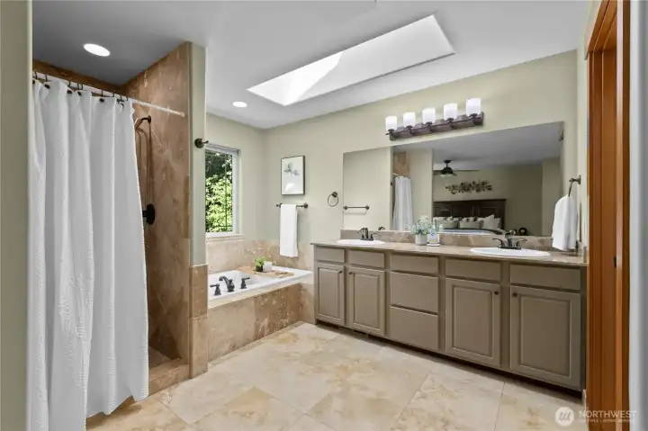Spa-like primary bath with soaking tub, tiled walk-in shower, dual vanities, and skylight overhead.